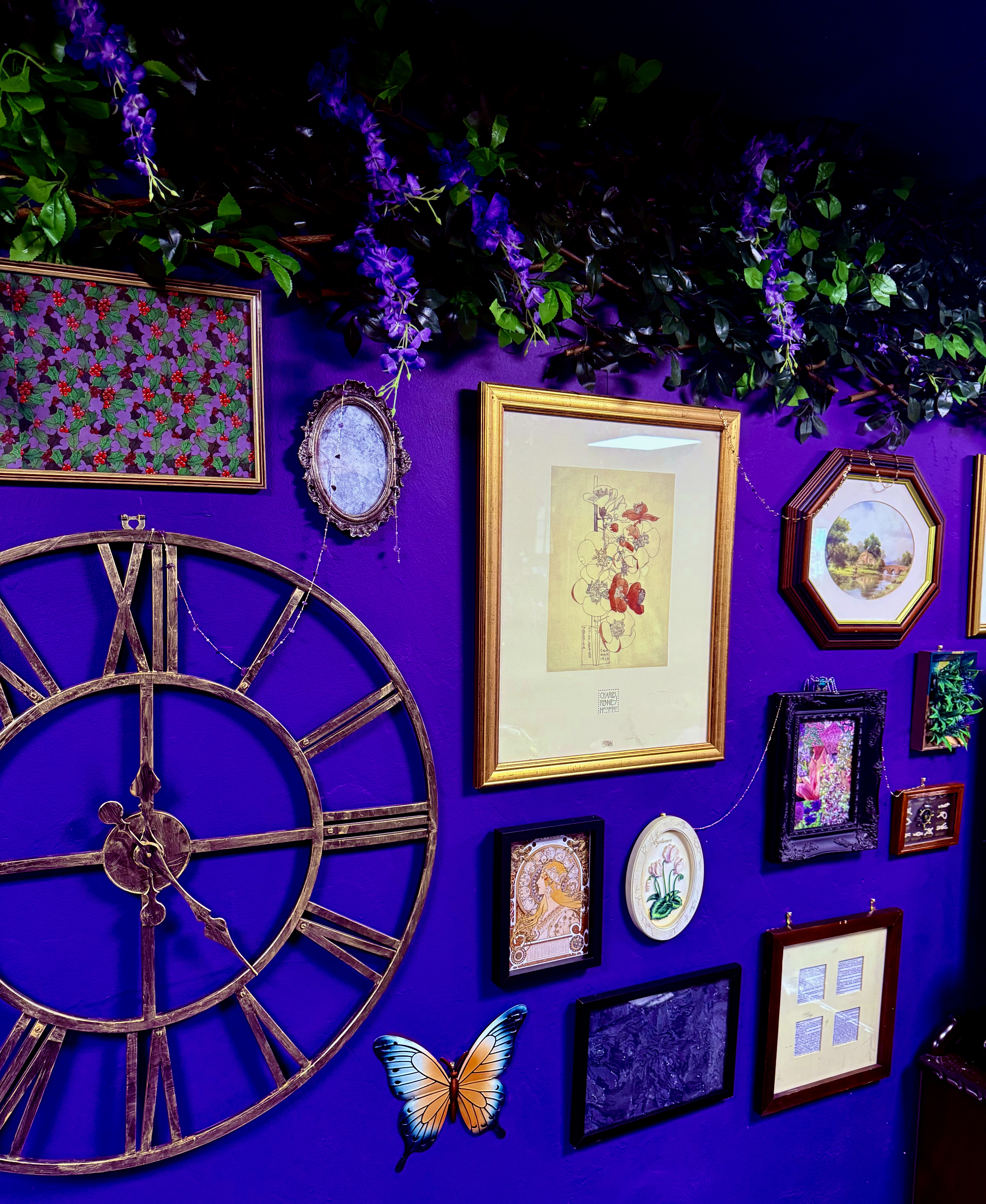 A purple wall hung with gilt picture frames, a giant wooden clock and cascading wisteria