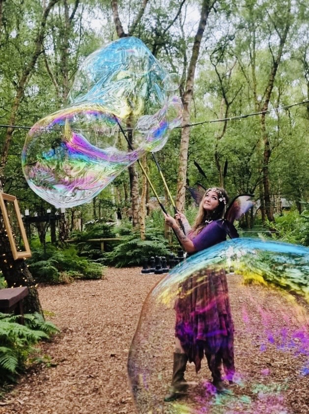 A winged fairy character drawing enormous soap bubbles through a woodland glade