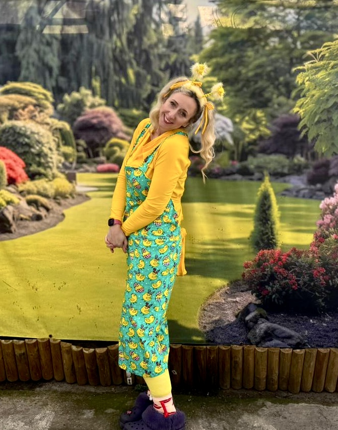 A party host in duckling-print dungarees and yellow ribbons in a spring garden
