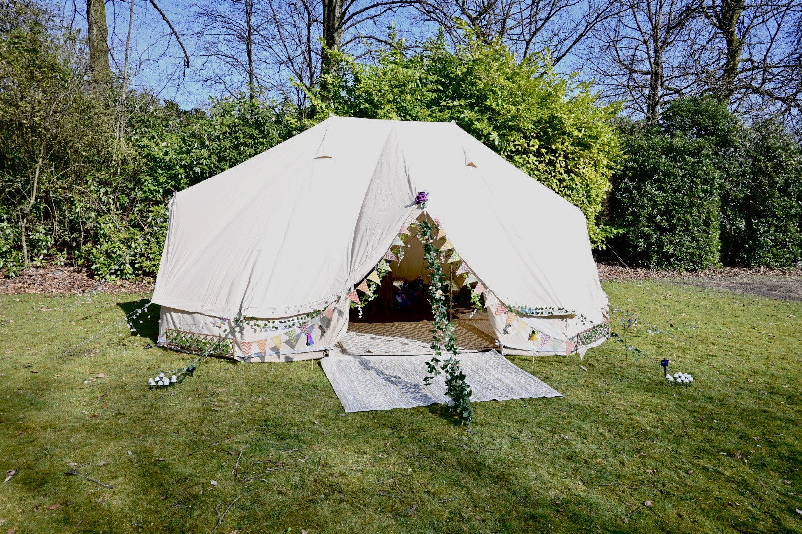 A bell tent set up on a lawn, trimmed with bunting and a garland of flowers