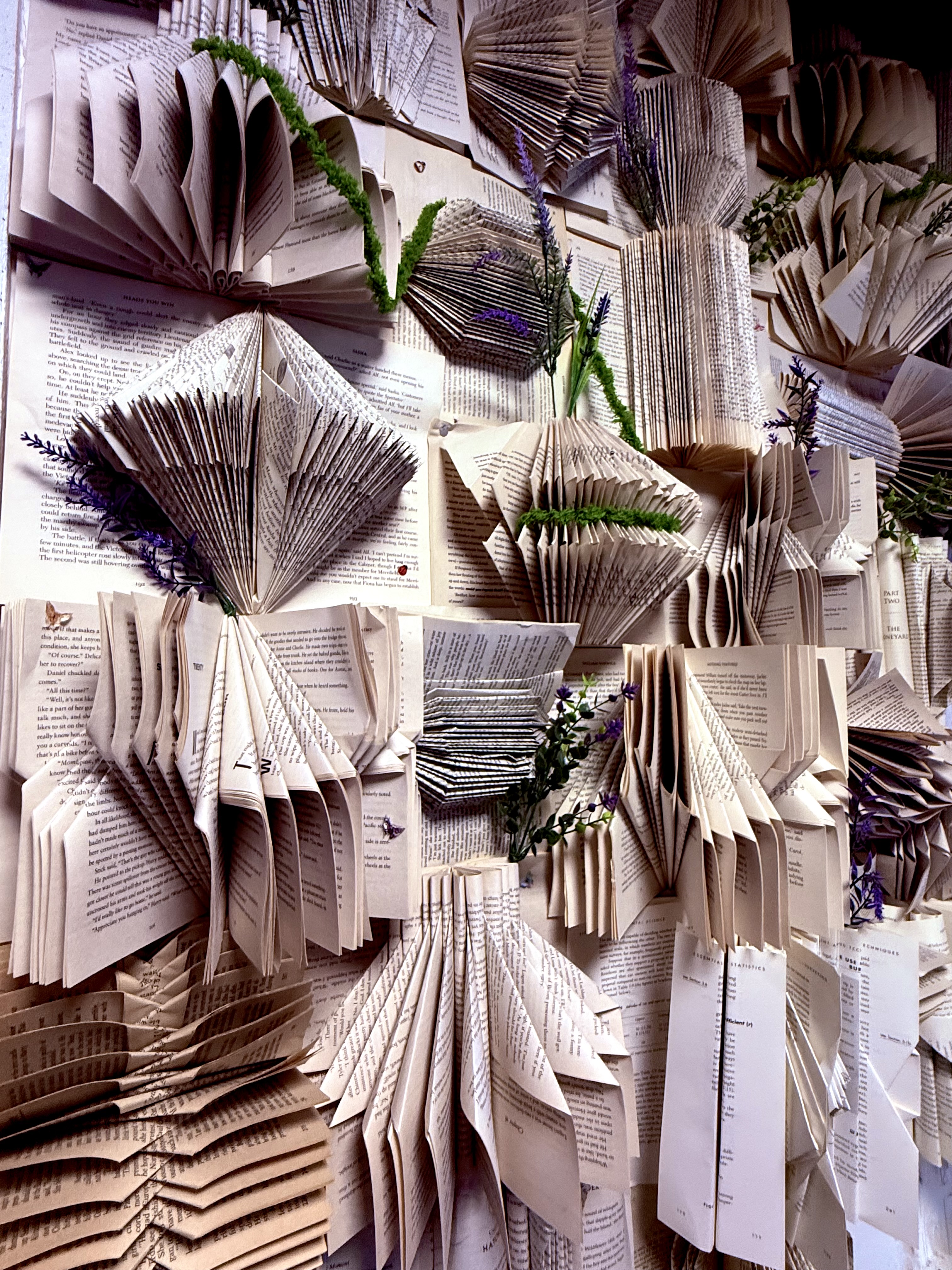 A wall of folded book pages dressed with sprigs of lavender