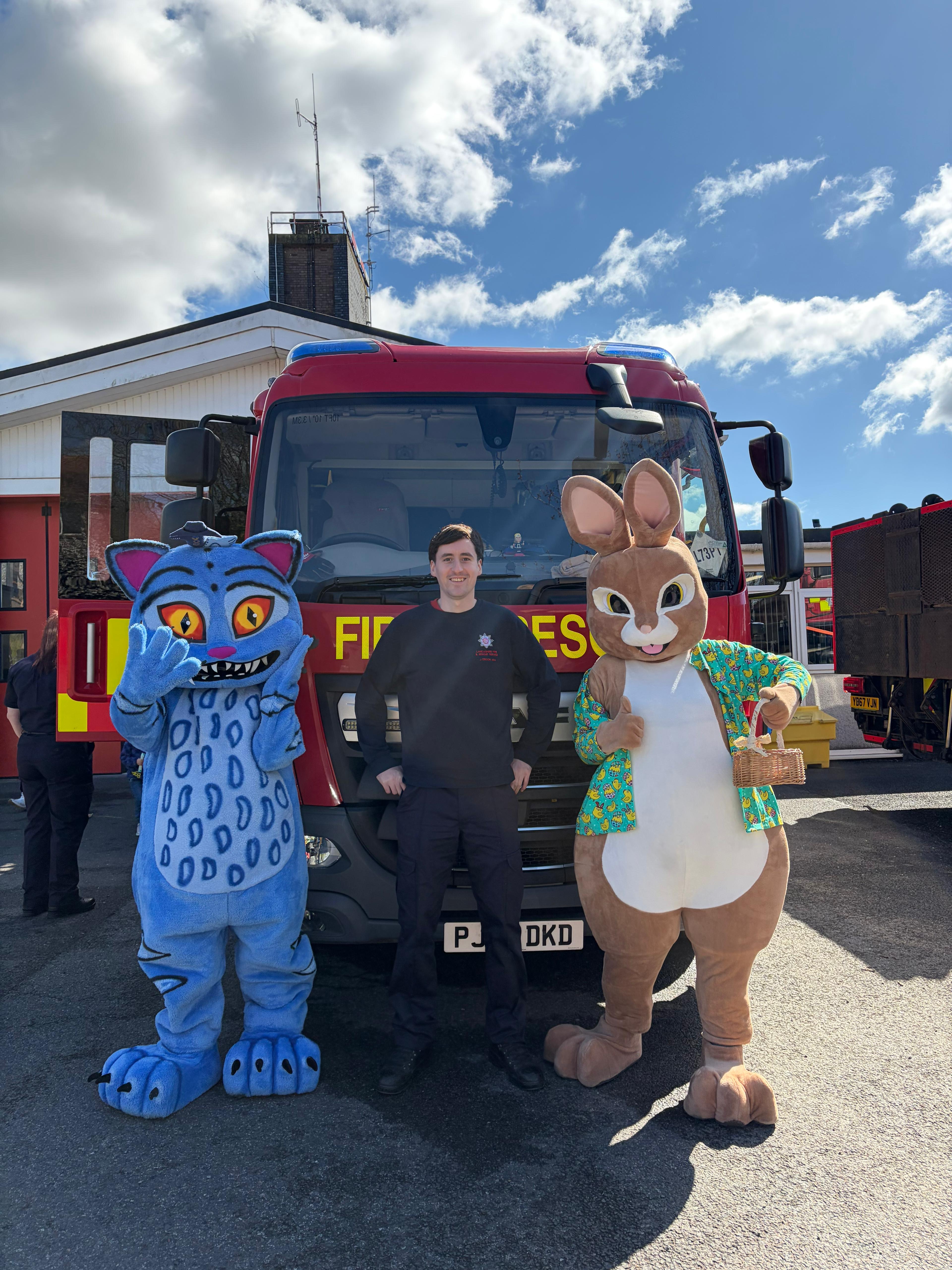Two costumed mascots posing with a firefighter in front of a fire engine
