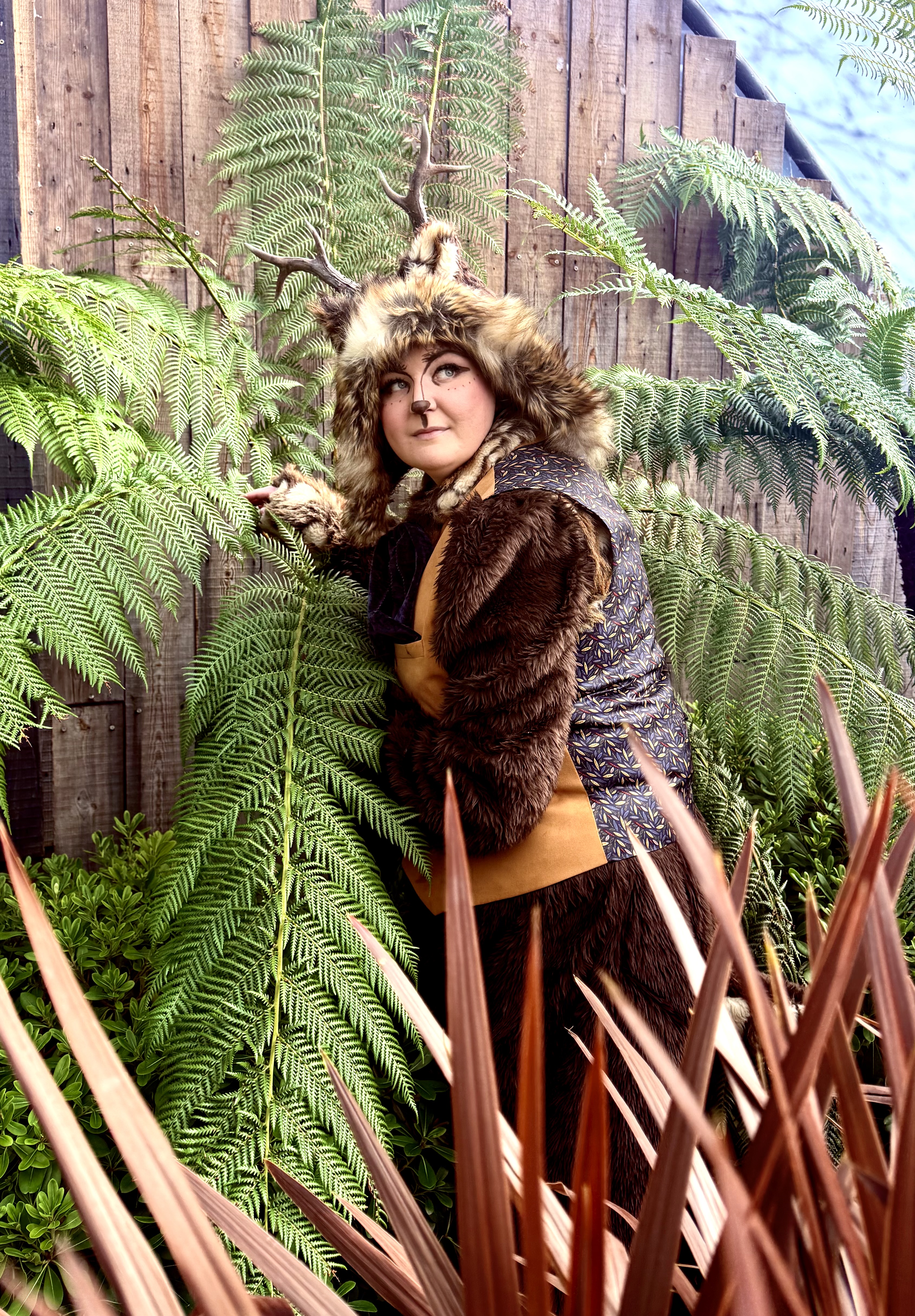 An antlered woodland character peering out from among tall tree ferns