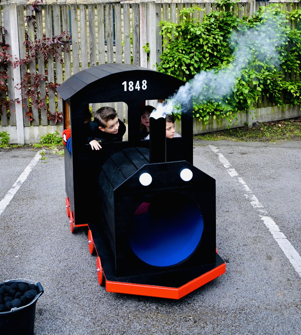 Children riding a handmade wooden steam engine puffing smoke