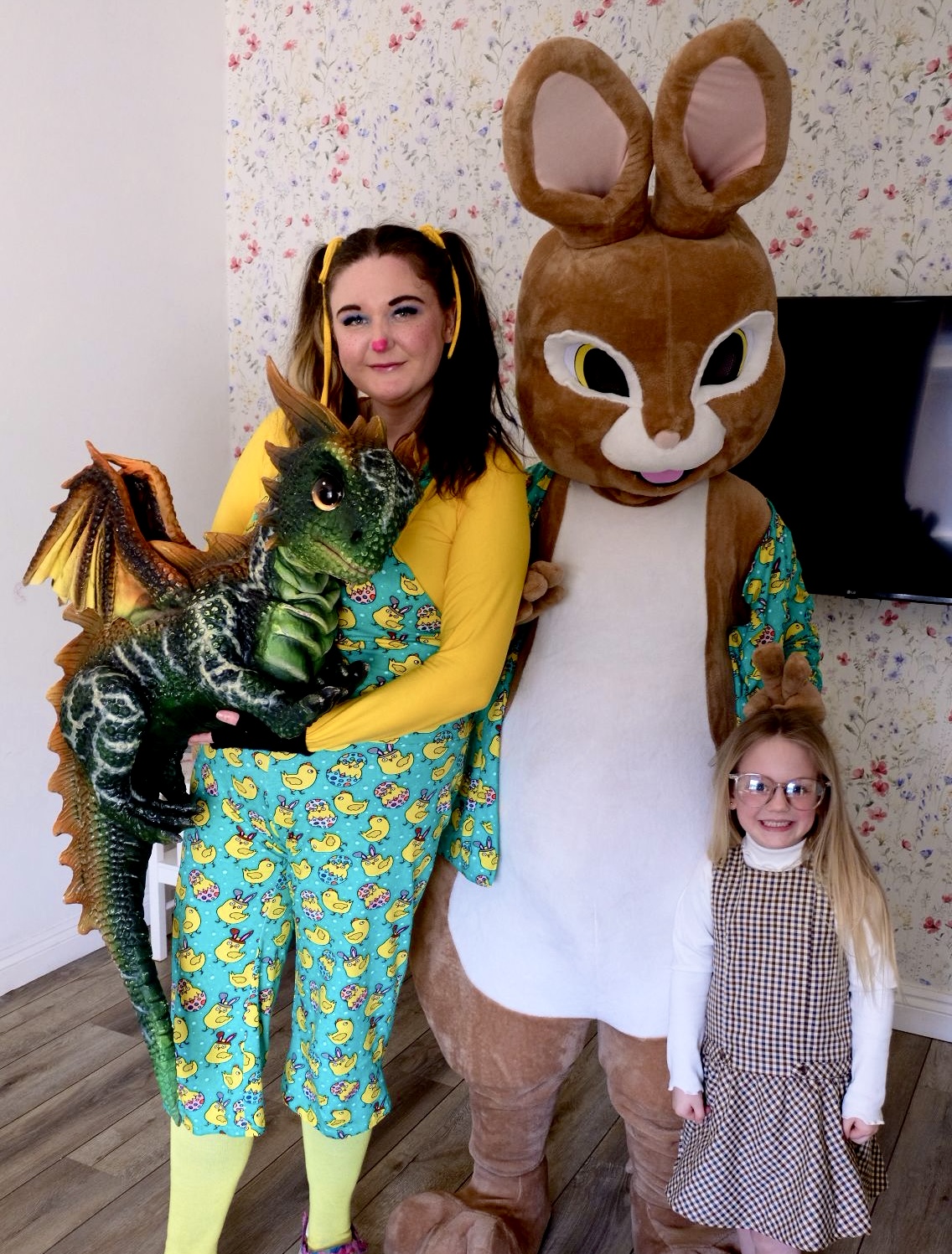 A host holding a lifelike green dragon beside a giant rabbit character and a delighted child