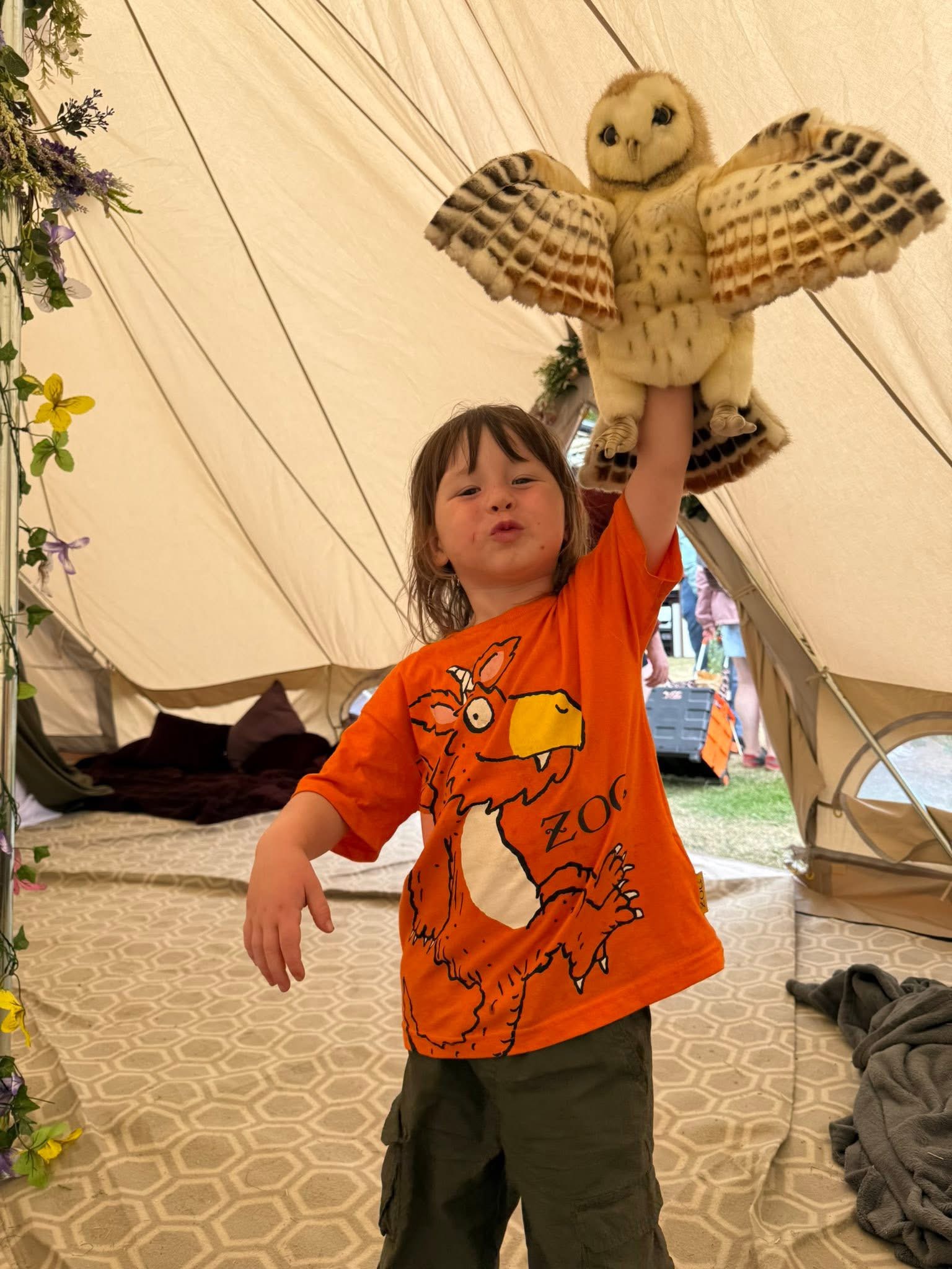 A child holding a barn owl puppet aloft inside a flower-trimmed tent